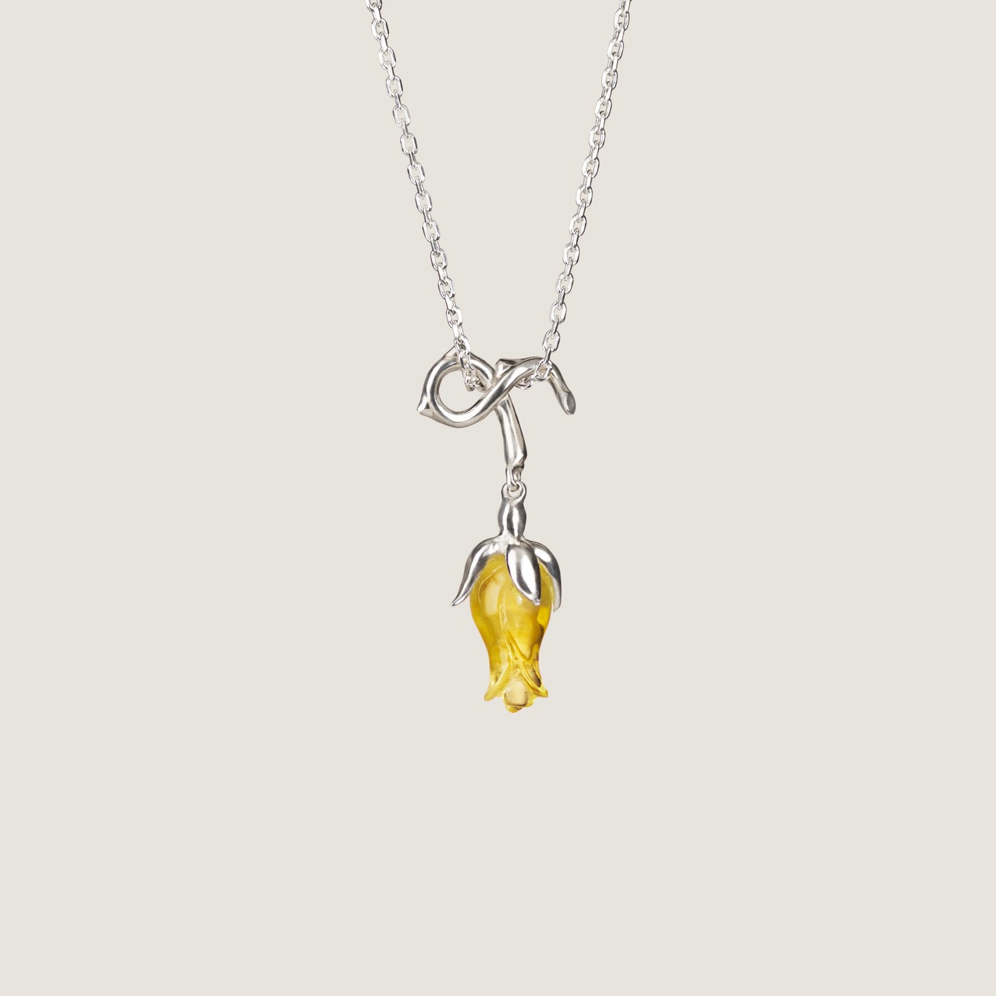 A silver necklace with a yellow rose-shaped pendant, displayed against a white background.
